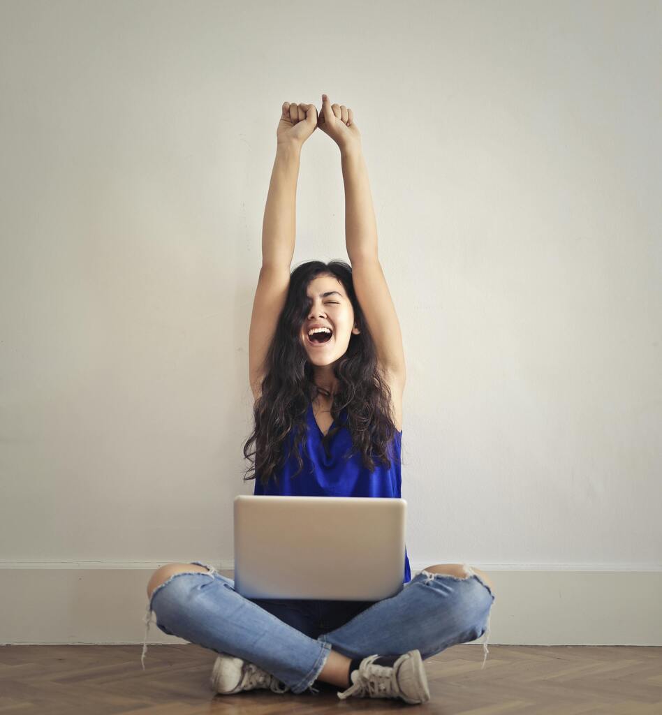 pexels-photo-3807737-3807737 Happy woman with laptop, celebrating success indoors. Arms raised in triumph.